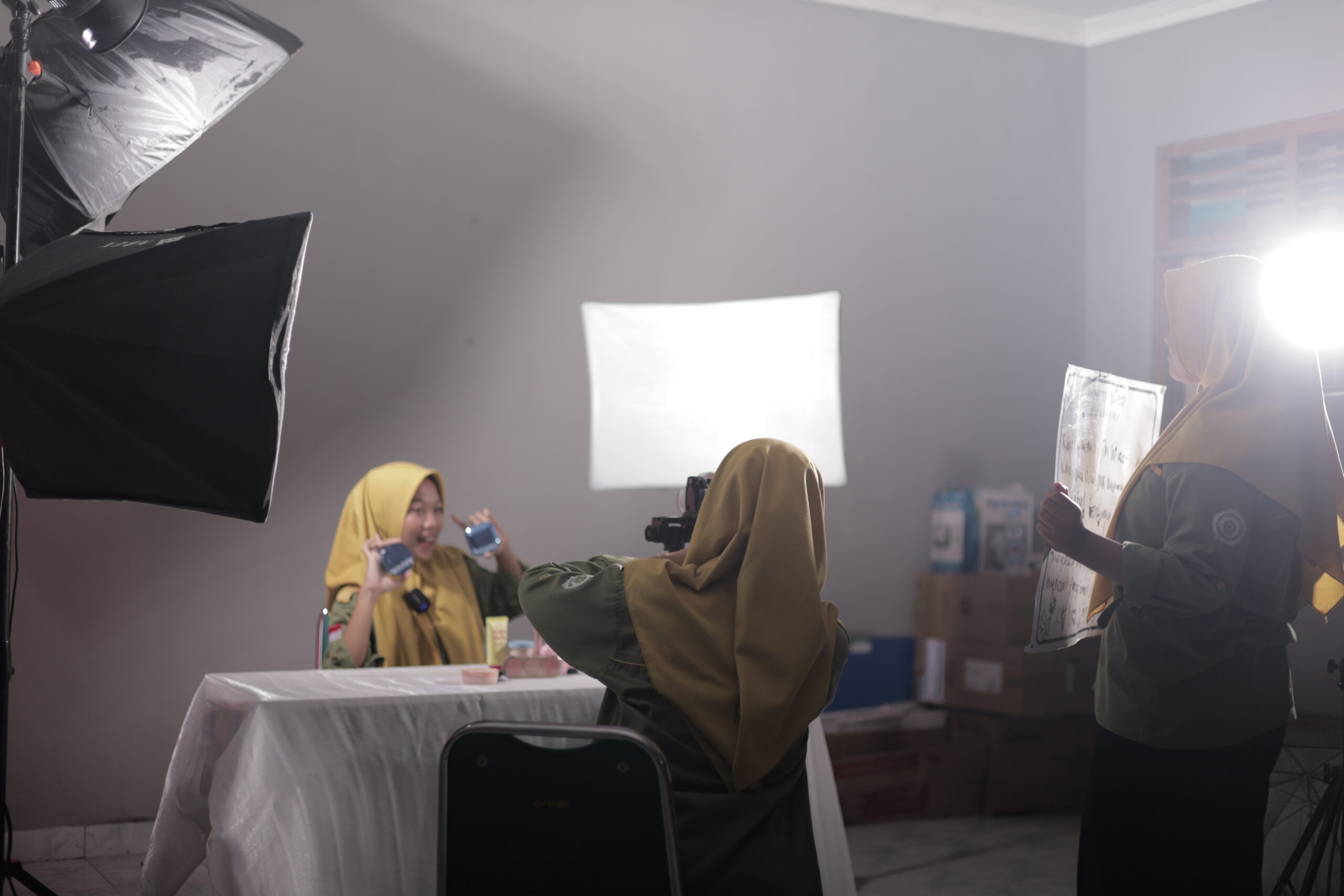 Siswa SMK Muhammadiyah 2 Bantul Program Keahlian Pemasaran sedang praktik live selling di kelas studio. Seorang siswa berperan sebagai host mempresentasikan produk skincare di depan kamera, sementara siswa lain mengoperasikan kamera dan pencahayaan profesional untuk mendukung siaran langsung di media sosial.